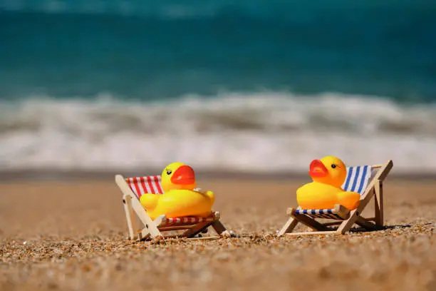 Two miniature deck chairs with rubber ducks at the shoreline of Pedn Vounder Beach, Cornwall on a sunny June day.