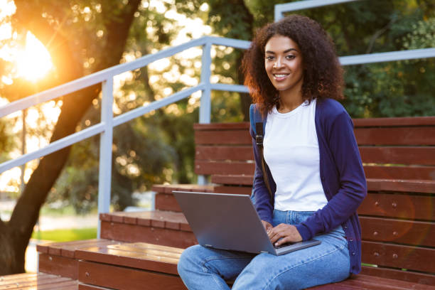 istock African young woman sitting outdoors in park on steps using laptop computer. 1329688857