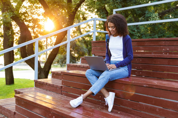 istock African young woman sitting outdoors in park on steps using laptop computer. 1329688972