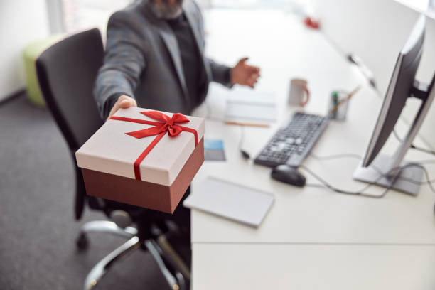 istock Happy office worker is holding a present and smiling 1329690368
