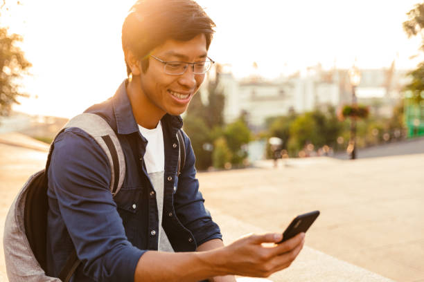 istock Cheerful asian male student in eyeglasses using smartphone 1329690603