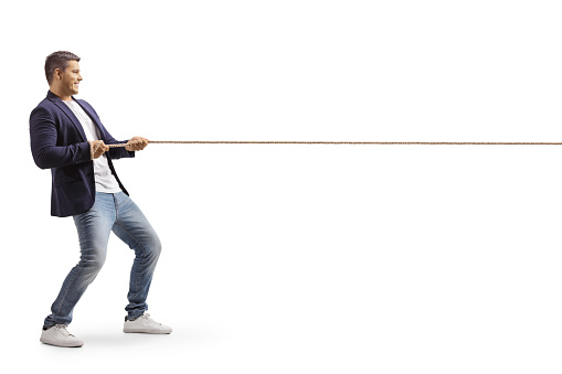Full length profile shot of a young casual man pulling a rope isolated on white background