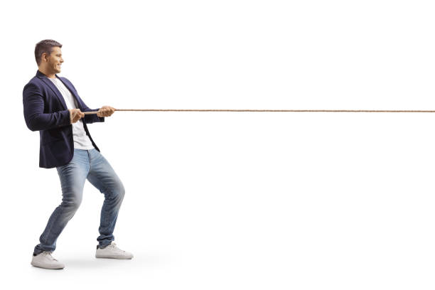 Full length profile shot of a young casual man pulling a rope Full length profile shot of a young casual man pulling a rope isolated on white background pulling stock pictures, royalty-free photos & images