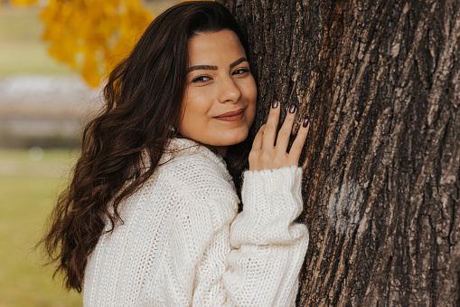 Close-up of peaceful young woman hugging tree in autumn park