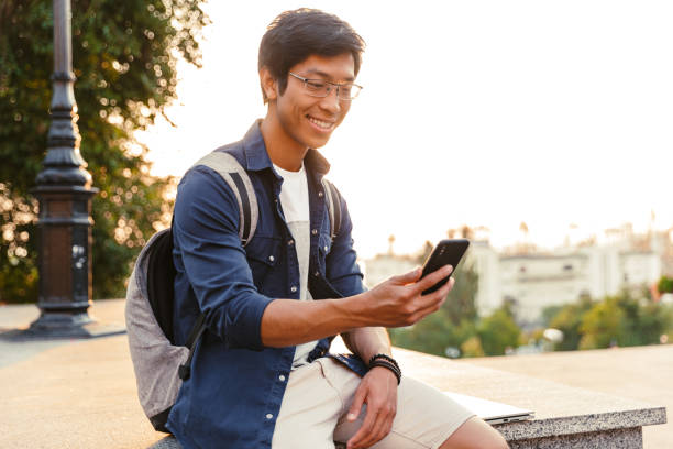 istock Joyful asian male student in eyeglasses using smartphone 1329691950