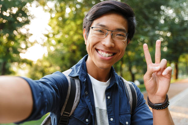 estudiante masculino asiático satisfecho en anteojos haciendo selfie - peace on earth audio fotografías e imágenes de stock