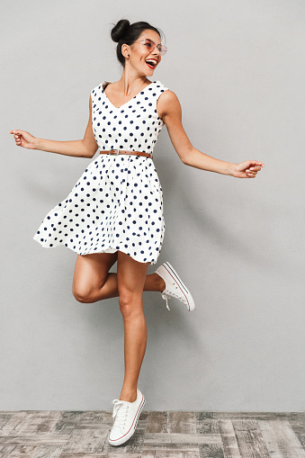 Full length portrait of a happy young woman in summer dress isolated, jumping