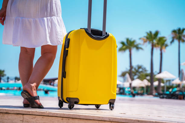 jeune femme avec ses bagages valise jaunes sur une belle plage de sable surplombant la mer par une journée ensoleillée. femme hipster en chemise en coton ample près de l’océan fond, gros plan - valise à roulettes photos et images de collection