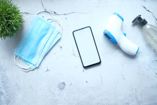 istock flat composition of smart phone, mask, thermometer and sanitizer on table 1329695620