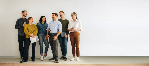 Diverse creative team looking happy Colleagues talking while standing at wall. Happy creative team standing at wall and discussing. coworker stock pictures, royalty-free photos & images