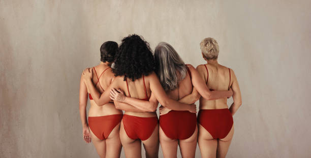 Rearview shot of four women of different ages embracing their natural bodies Rearview shot of four women of different ages embracing their natural and aging bodies. Group of women embracing each other while wearing red underwear and standing together in a studio. swimwear bikini top bikini bikini bottom stock pictures, royalty-free photos & images