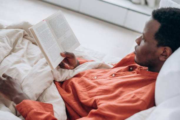 istock Black man in pajamas reads book lying in comfortable bed 1329697179