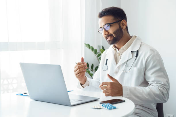 Portrait of indian man doctor talking to online patient on laptop screen stock photo