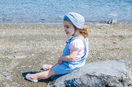 Little girl leaning on rock on beach of the St. Lawrence river in Les Méchins (Gaspésie) during day of summer