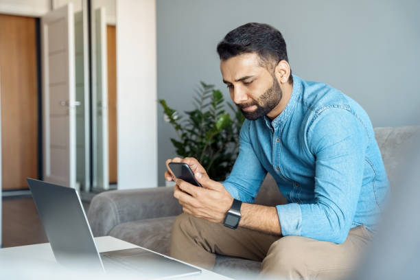 istock Serious indian business man using smartphone working laptop at home office 1329699272