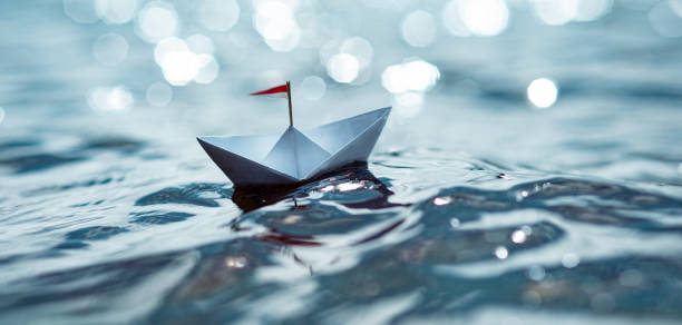 istock Paper ship sails on glittering water 1329699375