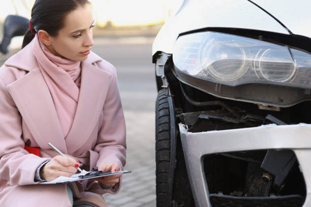 une experte remplissant des documents près d’une voiture cassée dans la rue - car inspector examining failure photos et images de collection