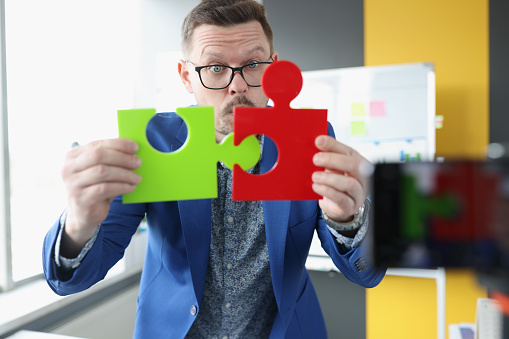 Male business coach connecting colorful puzzles in front of camera. Online business education concept