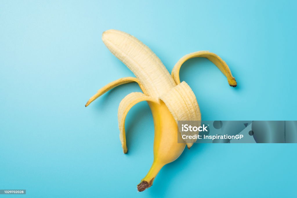 Top view photo of one peeled ripe banana in the middle on isolated pastel blue background Banana Stock Photo
