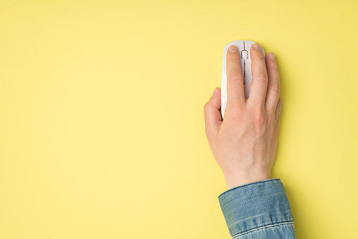 First person top view photo of female hand with white computer wireless mouse on isolated yellow background with copyspace