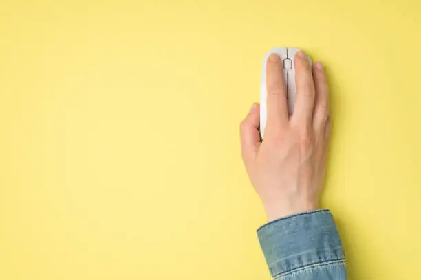 Photo of First person top view photo of female hand with white computer wireless mouse on isolated yellow background with copyspace