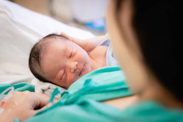 病院で人生の最初の日を眠る彼女の生まれたばかりの赤ちゃんを保持している若い母親, 愛と母の日の概念. - 誕生 ストックフォトと画像