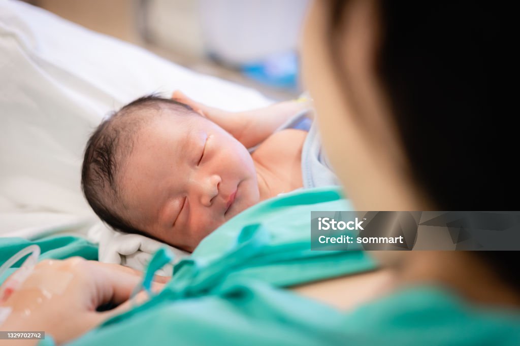 Young mother holding her newborn baby who sleep first days of life at hospital, love and Mother’s Day concept. Childbirth Stock Photo