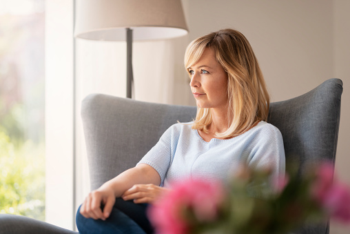 Shot of attractive middle aged woman daydreaming while relaxing on an armchair at home.
