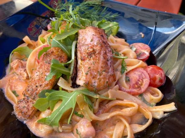 Grilled salmon with red cream sauce on pasta and rocket tomatoes stock photo