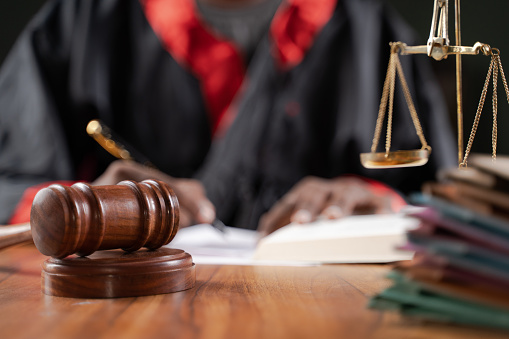 Focus on judge gavel, Unrecognizable judge busy writing verdict or making notes from the book with gavel and balance scale on table