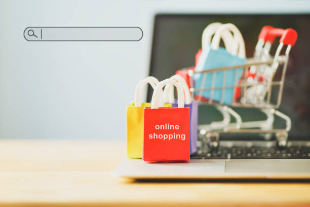 small red shopping paper bag on notebook and blurred cart, search bar beside with copy space, online shopping concept, e-commerce, buying or selling goods or services online over the internet pequeña bolsa de papel rojo de la compra en el cuaderno y el carro borroso, barra de búsqueda al lado con el espacio de la copia, concepto de la compra en línea, e-commerce, compra o venta de mercancías o de servicios en línea a través de internet