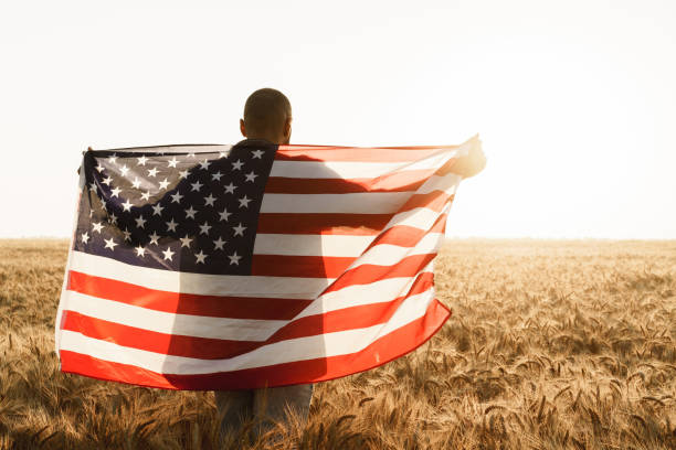 istock Young man holding American flag on back while standing in wheat field 1329709469