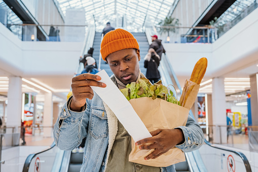 Hombre negro sorprendido mira el total de recibos con comida en el centro comercial photo