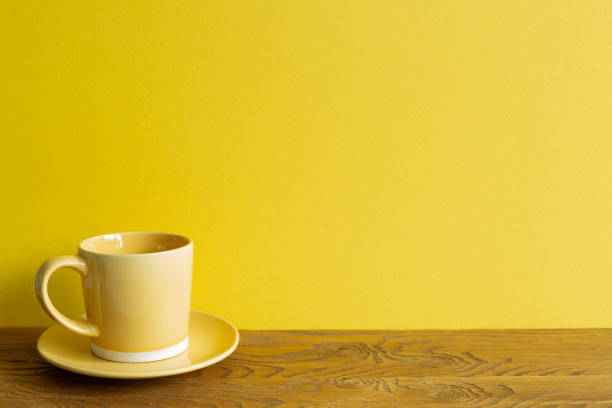 Yellow coffee cup on wooden table. yellow wall background. copy space