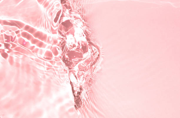Trendy abstract summer nature background. Pink liquid colored clear water surface texture with splashes bubbles. Defocused transparent clear pink water waves in sunlight