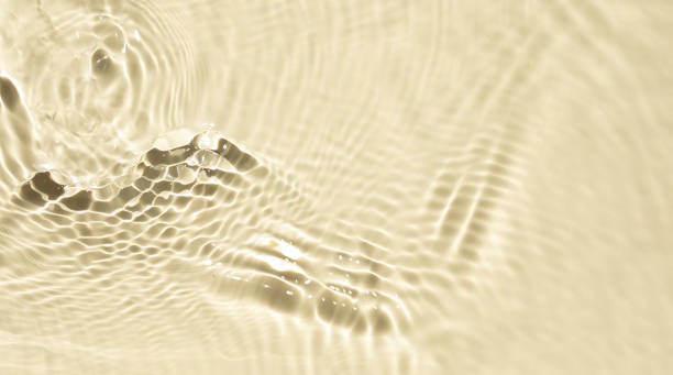 Yellow liquid colored clear water surface texture with splashes bubbles. Defocused transparent clear water waves in sunlight. Trendy abstract summer nature background with copy space.