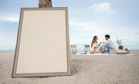 Couple at the background enjoying a romantic dinner at the beach and blank menu board to write your message - Copy space