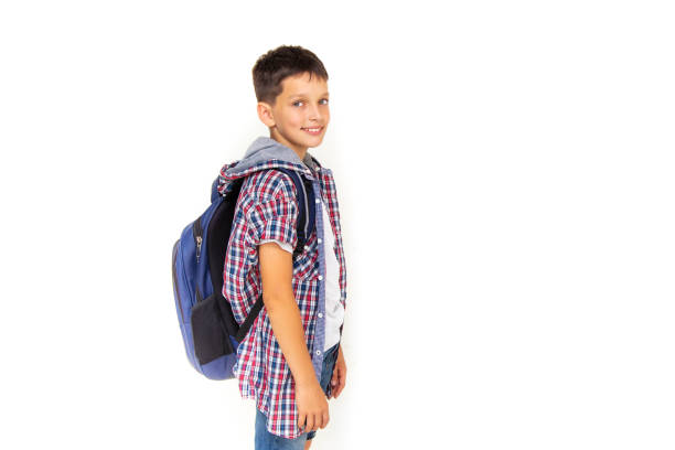 menino adolescente de 11 anos de idade estudante olhando para a câmera em fundo branco com mochila e sorrindo. vestido com camisa xadrez e camiseta branca, espaço de cópia - 10 11 years cheerful happiness fun - fotografias e filmes do acervo