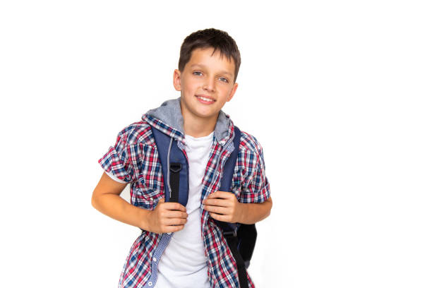 niño adolescente de 11 años colegial mirando la cámara sobre fondo blanco con mochila y sonriendo. vestido con camisa a cuadros y camisa blanca - 10 11 years little boys child happiness fotografías e imágenes de stock