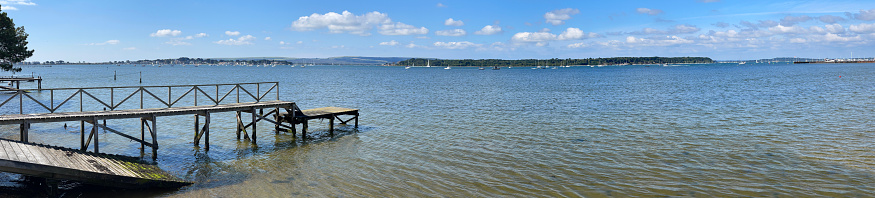 Summer high tide panorama with jetty looking towards Brownsea island at the water's edge of Poole Harbour, Dorset, England, UK.
