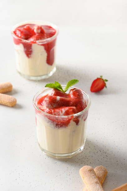 Layered dessert in glass jars with cookie savoyardi, mascarpone and whipped cream decorated strawberries Layered summer dessert in glass jars with cookie savoyardi, mascarpone and whipped cream decorated strawberries. Close up. Italian tiramisu with summer vibes on white. yogurt fruit biscotti berry fruit stock pictures, royalty-free photos & images