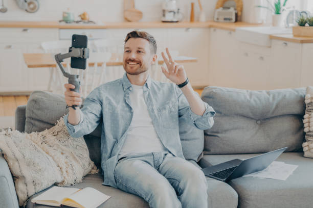 istock Positive young man showing peace sign during video call while sitting on couch 1329727215
