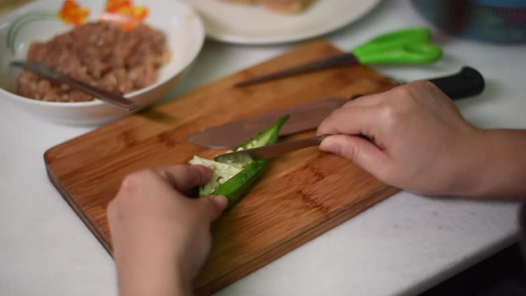 High angle view of woman use kitchen knife cutting and cleaning okra with spoon in living room