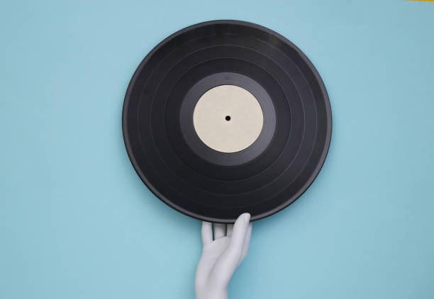 istock Mannequin's white hand holding  vinyl record on blue background. Top view 1329731107