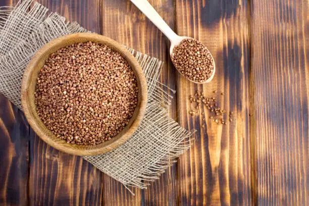 Photo of Raw buckwheat in the bowl on the rustic  wooden background. Top view.