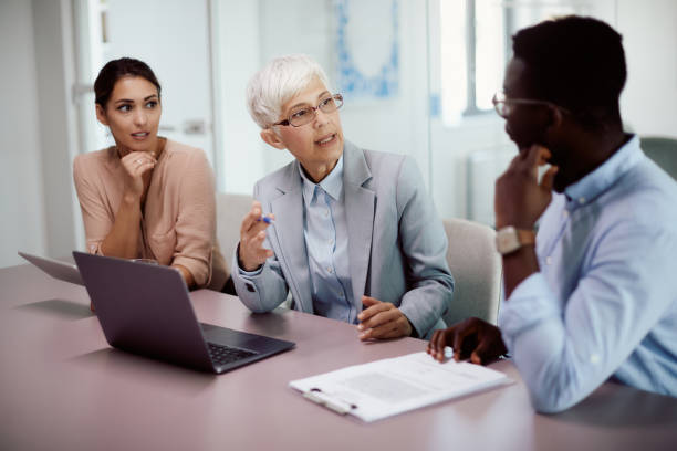 Mature businesswoman using laptop while communicating with her younger colleagues in the office.