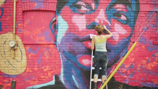 Young woman painting mural on the house