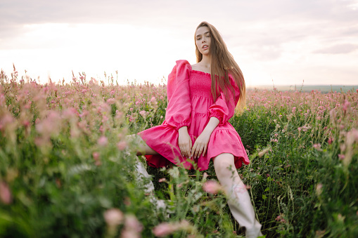 Stylish woman in a pink dress posing in the blooming field. Nature, vacation, relax and lifestyle. Fashion concept.