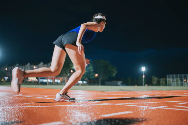 side view aerodynamic asian chinese female athletes sprint running at track and run towards finishing line at track and field stadium track rainy night - sports track track and field stadium sport night imagens e fotografias de stock