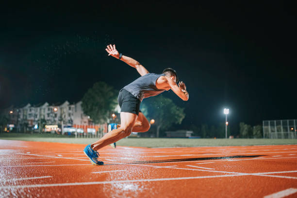side view aerodynamic asian chinese male athletes sprint running at track and run towards finishing line at track and field stadium track rainy night - sports track track and field stadium sport night imagens e fotografias de stock